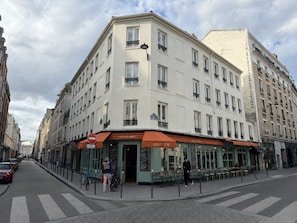 A corner building with a cafe named 'Cafe des Anges' on the ground floor, featuring outdoor seating and a bike rack.