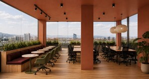 Ein moderner Büroarbeitsplatz mit einem langen Tisch, Stühlen und einer Sitzecke mit Blick auf die Stadtlandschaft.