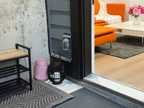 A modern interior with a wooden table, metal bench, pink baskets, a black lantern, and a grey sofa in a bright room.