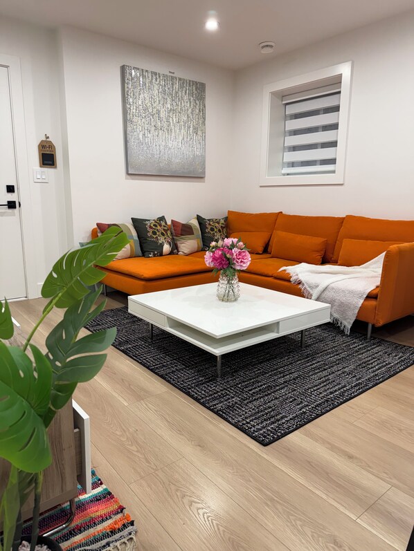 A modern living room with a white coffee table, orange sofa, and a black rug.