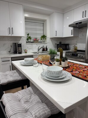 A modern kitchen with white cabinetry, a central island with dining ware, a microwave, and a stove.