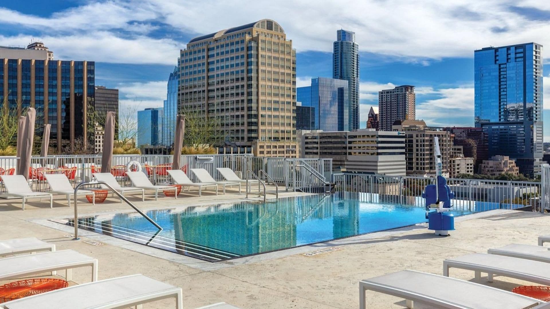 A rooftop pool with lounge chairs and a city skyline in the background.