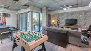 A modern living room with a foosball table, a sofa, a TV, and a balcony with glass doors.