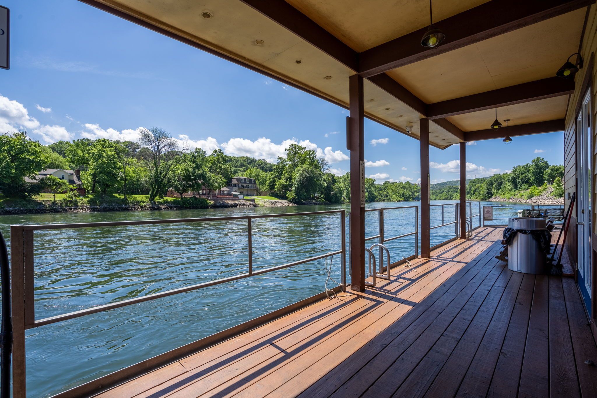 A covered deck with a view of a river, wooden railing, and a metal railing.