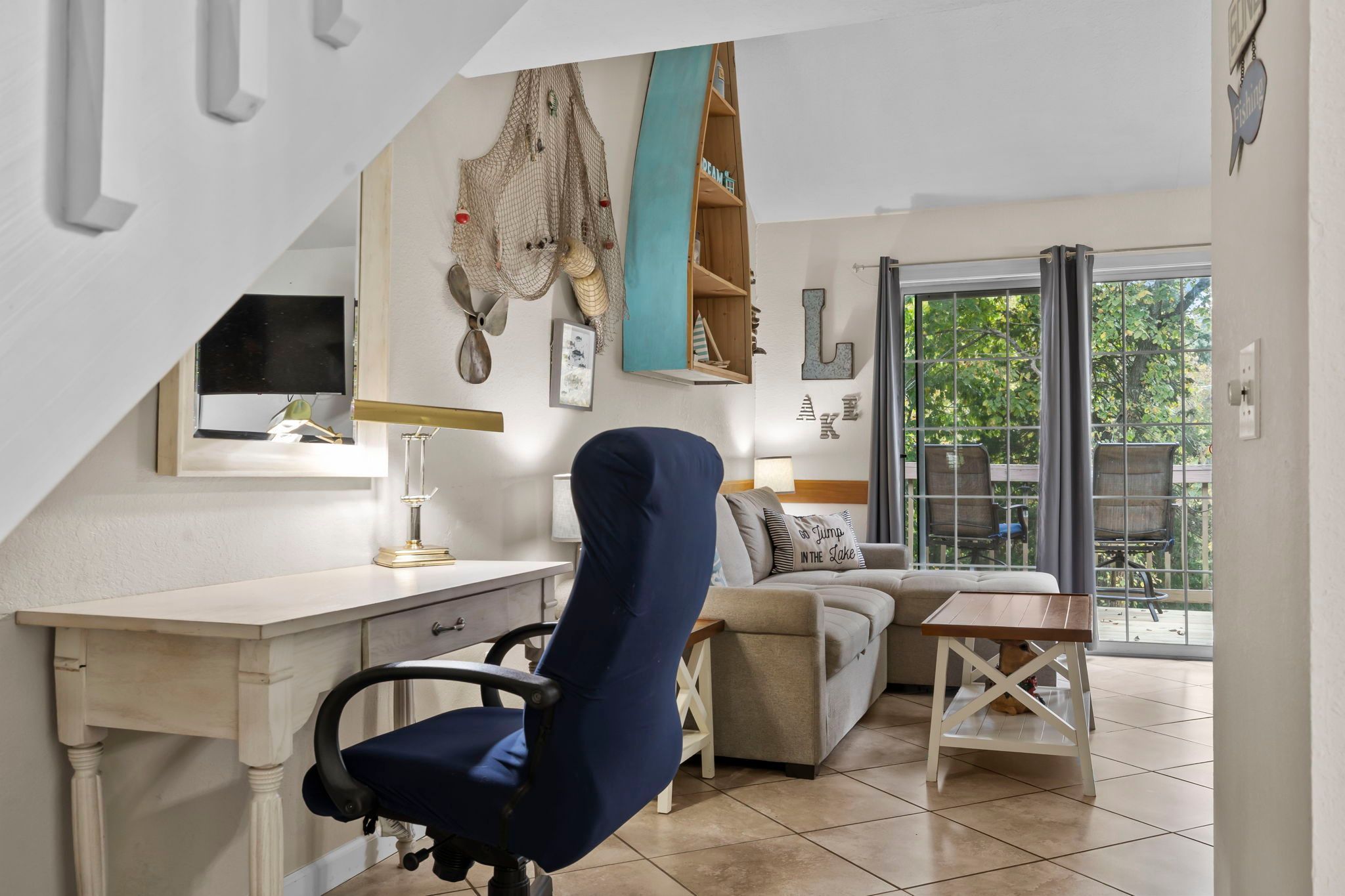 Une pièce comprenant un bureau, une chaise, un canapé et donnant sur l’extérieur grâce à une porte vitrée.