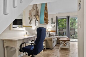 Ein Zimmer mit Schreibtisch, Stuhl, Sofa und Blick durch eine Glastür.