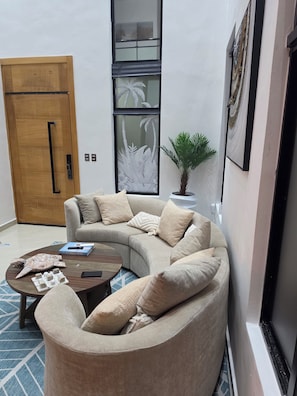 A modern living room with a curved sofa, a coffee table, and a potted plant. - PC Casa Palma- 3BDR in tranquil spot w/ Pool, Pergola, A/C, Parking & Security. (Estados Unidos)