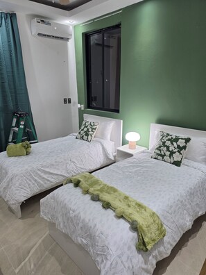 Ein Hotelzimmer mit zwei Betten, einem Fenster, einer Klimaanlage und einem grünen Vorhang.