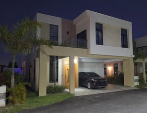 A modern two-story house with a garage, a car parked inside, and a well-maintained lawn. - PC Casa Palma- 3BDR in tranquil spot w/ Pool, Pergola, A/C, Parking & Security. (Estados Unidos)