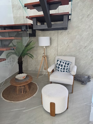 A modern living room with a glass staircase, a round wooden table, a white armchair with a patterned pillow, and a floor lamp. - PC Casa Palma- 3BDR in tranquil spot w/ Pool, Pergola, A/C, Parking & Security. (Estados Unidos)