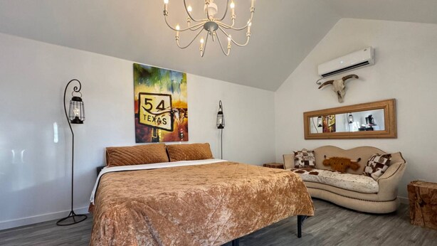 A bedroom with a large bed, a sofa, a chandelier, and a wall-mounted air conditioner. - "The Ft Worth" Romantic Tiny Home Near Wineries (Weatherford)