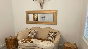 A room with a sofa, two wooden stools, a mirror, and a wall-mounted animal skull. - "The Ft Worth" Romantic Tiny Home Near Wineries (Weatherford)