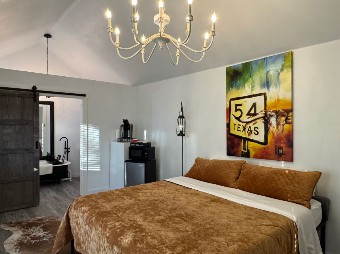 Une chambre avec un grand lit, un lustre, un tableau représentant un panneau de signalisation routière du Texas, et une salle de bain visible au fond.