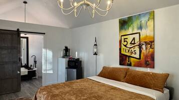 Une chambre avec un grand lit, un lustre, un tableau représentant un panneau de signalisation routière du Texas, et une salle de bain visible au fond.