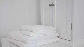 Une pile de serviettes blanches est posée sur une surface blanche, à côté d’une porte blanche dotée d’une poignée argentée.