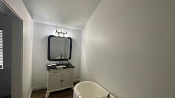 A bathroom with a white vanity, a mirror, a bathtub, and a wooden ceiling beam.