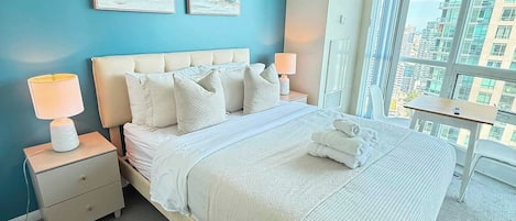 A hotel room with a large bed, two bedside tables, a nightstand, a window with a city view, and two wall-mounted artworks.