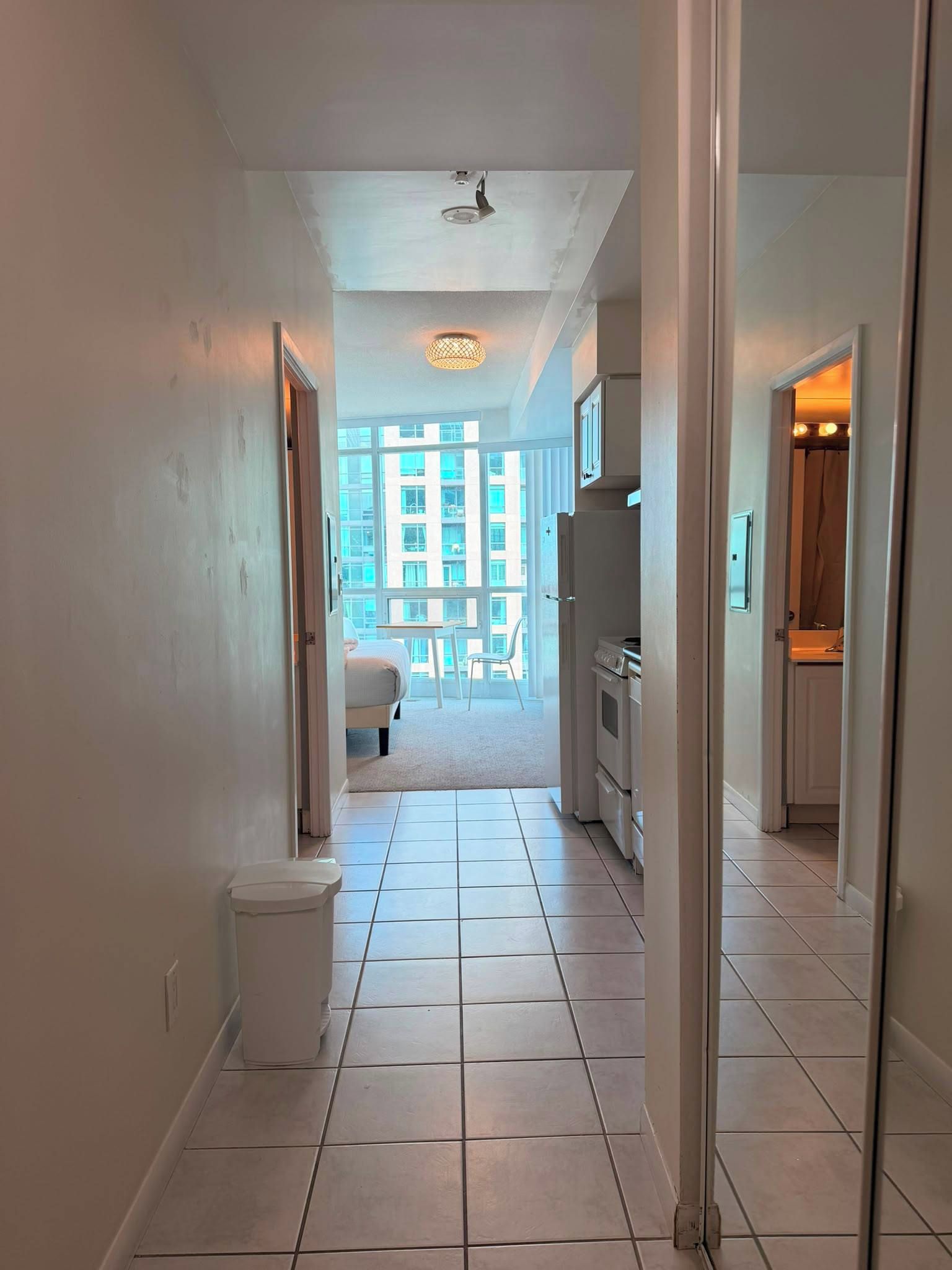 A corridor with a tiled floor leading to a bedroom with a bed and a window.