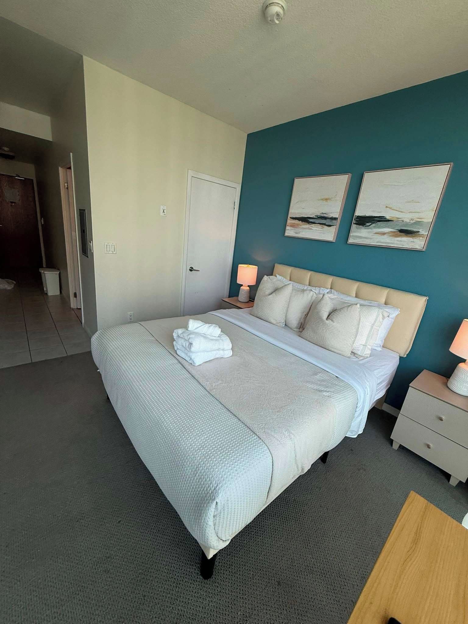 A hotel room with a large bed, two bedside lamps, a door, and two wall art pieces.