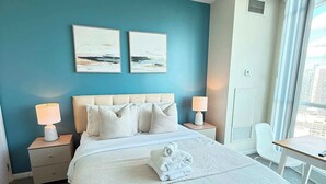 A hotel room with a large bed, two bedside lamps, a desk, and a window with a city view.