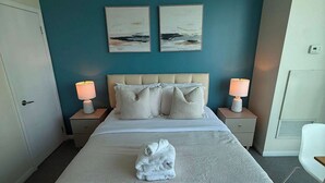 A hotel room with a large bed, two bedside tables with lamps, a door, and two wall-mounted paintings.