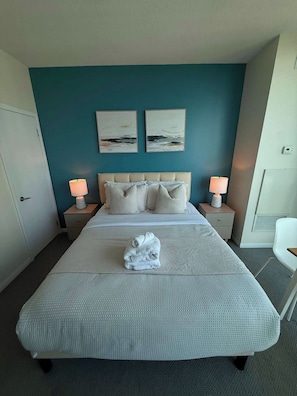 A hotel room with a large bed, two bedside tables with lamps, a door, and two wall-mounted paintings.