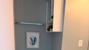 A compact bathroom with a toilet, a small trash bin, a toilet paper holder, and a shelf with a plant.
