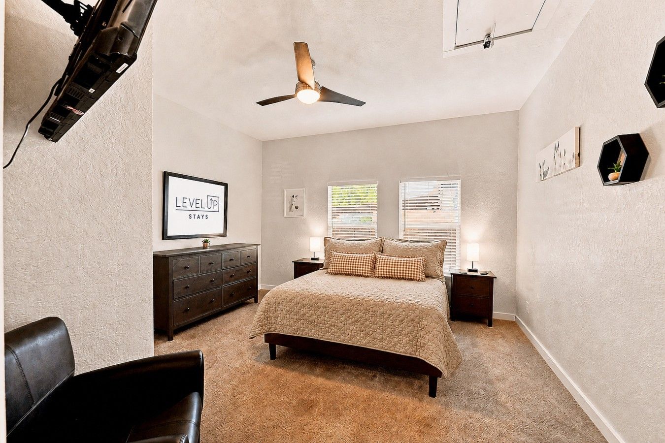 A bedroom with a bed, a dresser, a chair, a ceiling fan, and wall-mounted artwork.