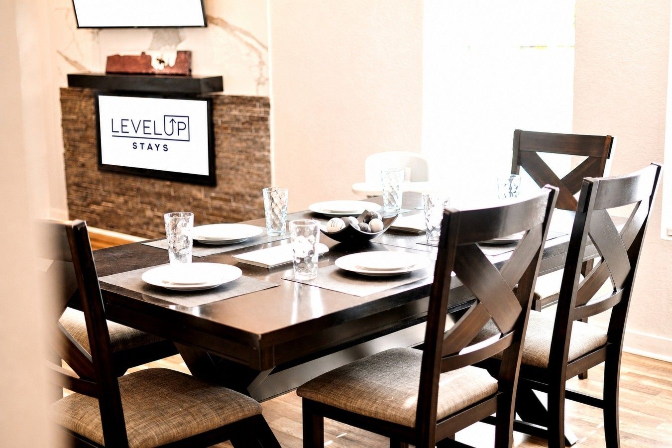 A dining table set with plates, glasses, and a bowl of fruit, with a sign reading 'LEVEL UP STAYS' above it.