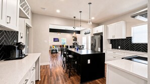A modern kitchen with a central island, bar stools, and a dining area with a sofa and chairs. - Fireplace~Outdoor Games~Near Downtown~Grill (San Antonio)