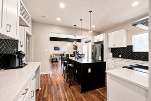 Una cocina moderna con una isla central, taburetes de bar y un área de comedor con sofá y sillas.