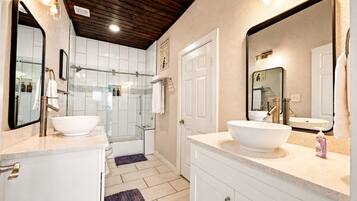 Un baño moderno con dos lavamanos grandes de color blanco, una cabina de ducha con mampara de cristal y techo de madera.