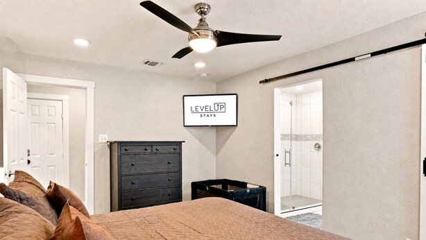 A bedroom with a bed, a dresser, a ceiling fan, a framed sign, and a shower area. - Fireplace~Outdoor Games~Near Downtown~Grill (San Antonio)