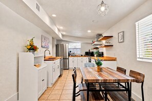 Una cocina moderna con armarios blancos, una mesa de comedor de madera y una lámpara colgante.