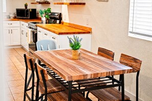 Uma mesa de jantar de madeira com cadeiras, um vaso de planta e uma cozinha ao fundo.