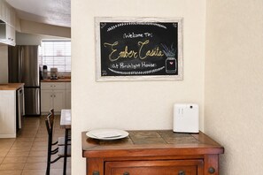 Uma cozinha com uma lousa, uma mesa de madeira e um aparelho branco na bancada.