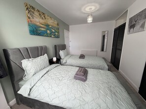 A hotel room with two beds, a painting on the wall, a ceiling light, and a window with shutters. - Home in Heart of Leeds /drive way parking 10 minutes to city centre (Leeds)