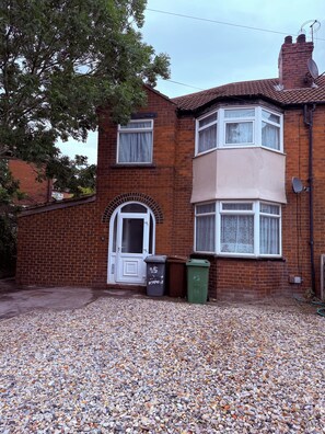 A two-story brick house with a bay window, a front door, and a gravel driveway. - Home in Heart of Leeds /drive way parking 10 minutes to city centre (Leeds)