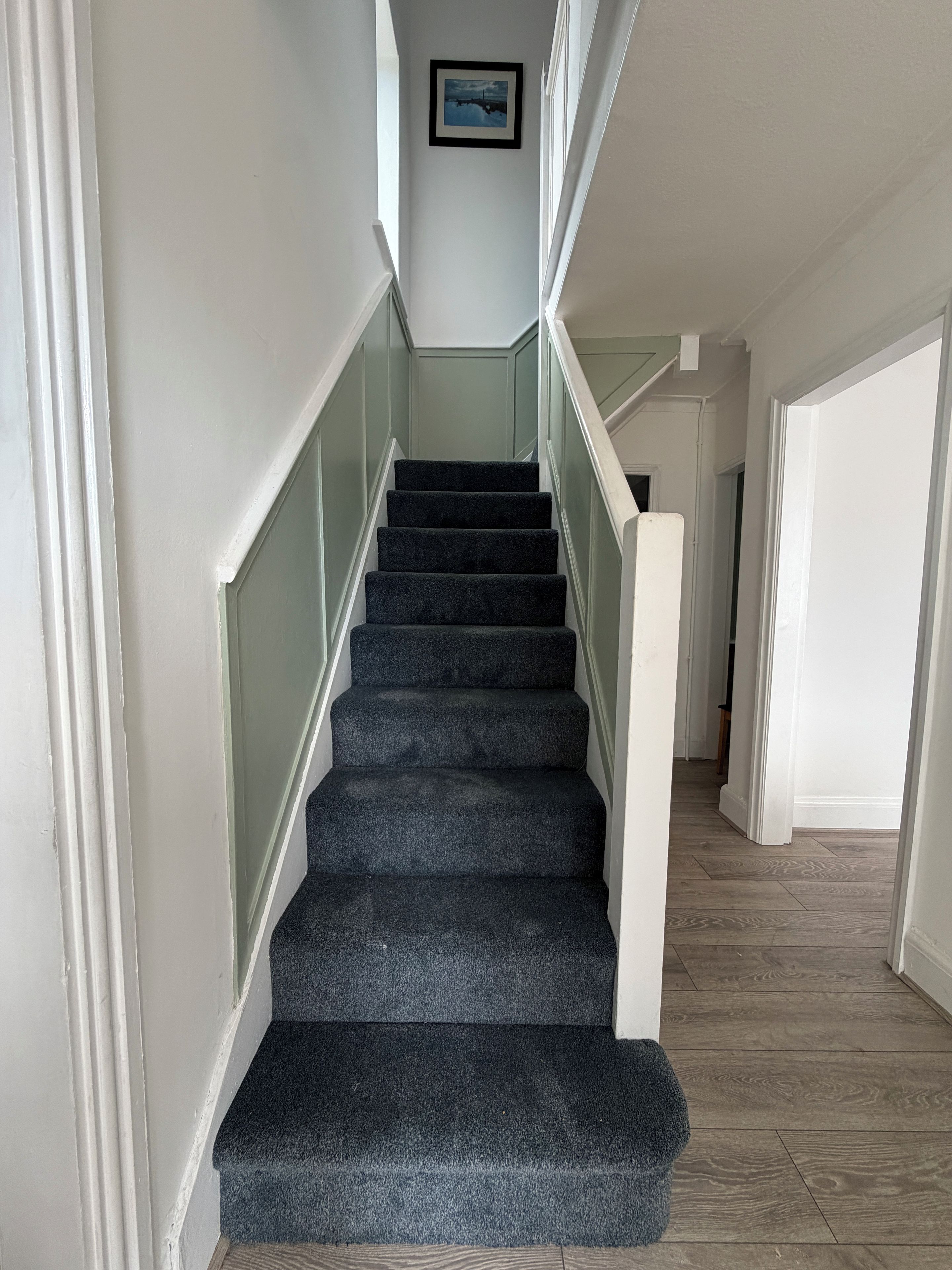 A staircase with a handrail, carpeted steps, and a picture on the wall.
