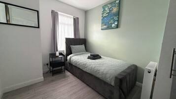 A bedroom with a bed, a nightstand, a painting, and a window with curtains.