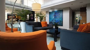 Een moderne lobby met zithoeken, een salontafel en een groot abstract schilderij aan de muur.