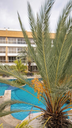 A swimming pool surrounded by palm trees and a building with large windows. - GoUppers® Lujo en Pampatar Margarita Real (Pampatar)