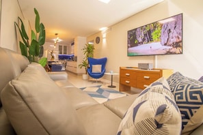 Een moderne woonkamer met een bank, een blauwe stoel, een houten kast en een flatscreen televisie aan de muur.