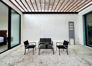 Una habitación moderna con un ventanal grande, una cama, una mesita con sillas y una puerta gris.
