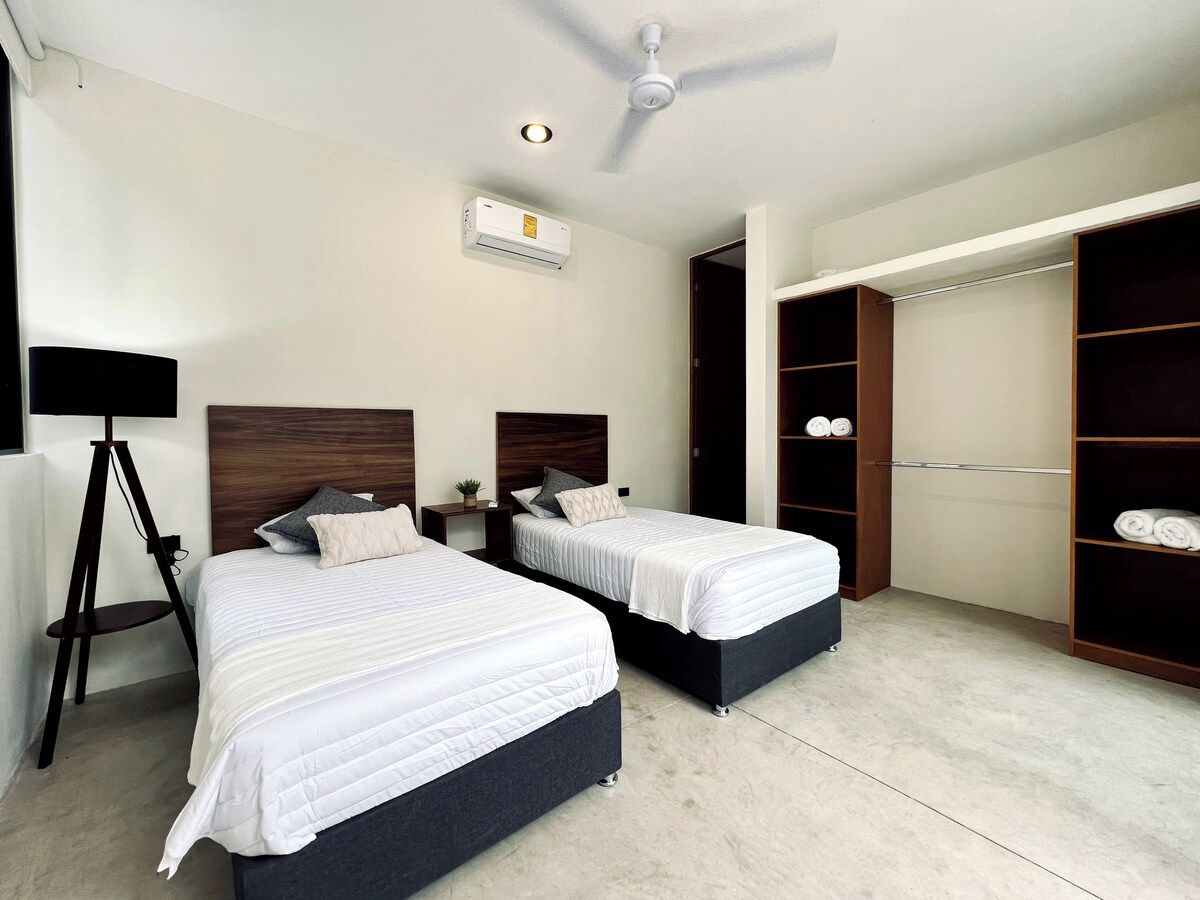 A hotel room with two beds, a ceiling fan, an air conditioning unit, a wardrobe, and a floor lamp.