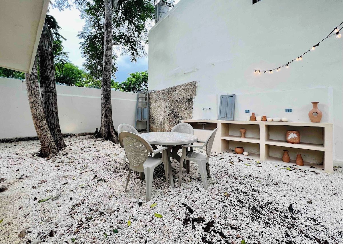 Un patio al aire libre con una mesa redonda y sillas, rodeado por un muro blanco y árboles.