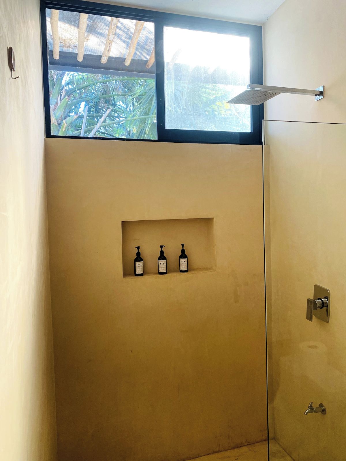 A shower area with a window above, a towel rack, and a shelf with three bottles.