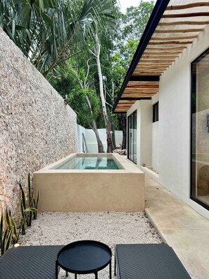 A modern outdoor pool area with a stone wall, a wooden pergola, and a seating area with a table and chairs. - Casa Álamo in Downtown Mérida: 1br+Private Pool (Merida)