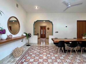 A dining area with a wooden table and chairs, a mirror on the wall, and a patterned rug. - Casa Álamo in Downtown Mérida: 1br+Private Pool (Merida)