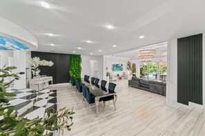 Un espace de restauration moderne avec une longue table et des chaises, un mur vert et une vue sur l’extérieur.